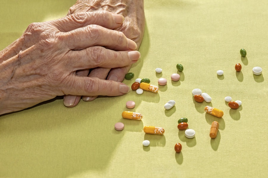 Arthritic hands beside an assortment of pills