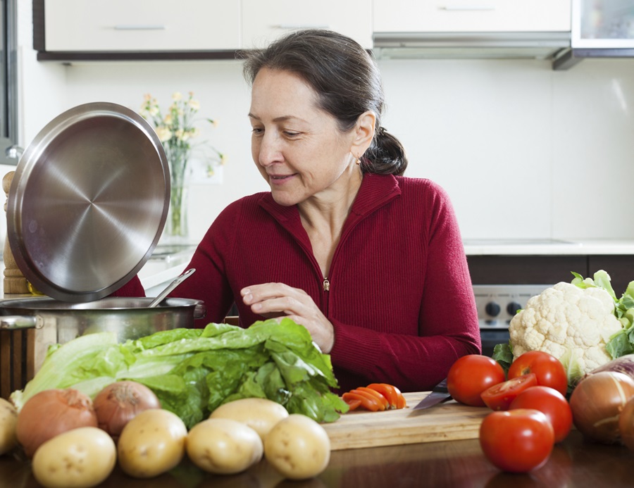 Older woman in kitchen with cooking pot and vegetables