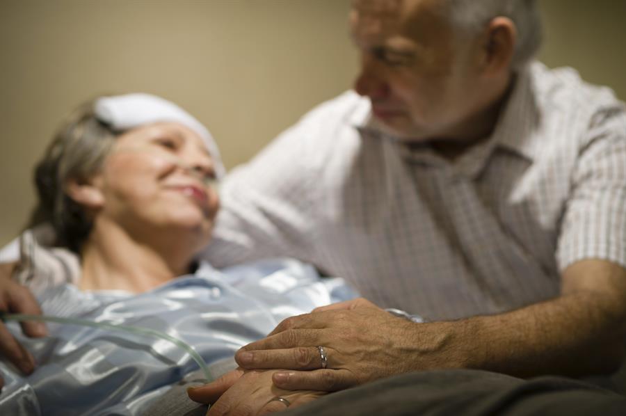 ailing woman in bed with bandage on her head, man looking at and embracing her, both smiling