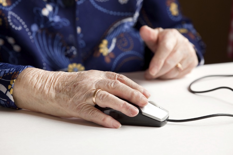 Older person's hand with wedding ring resting on computer mouse