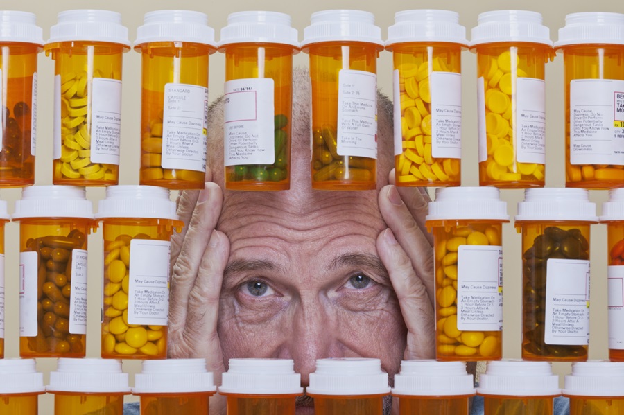 Senior man with an unhappy, confused expression looking through an opening in rows of prescription medication.