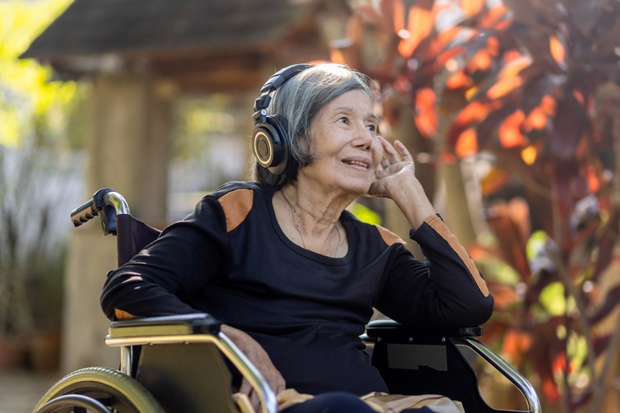 femme plus âgée en fauteuil roulant portant des écouteurs